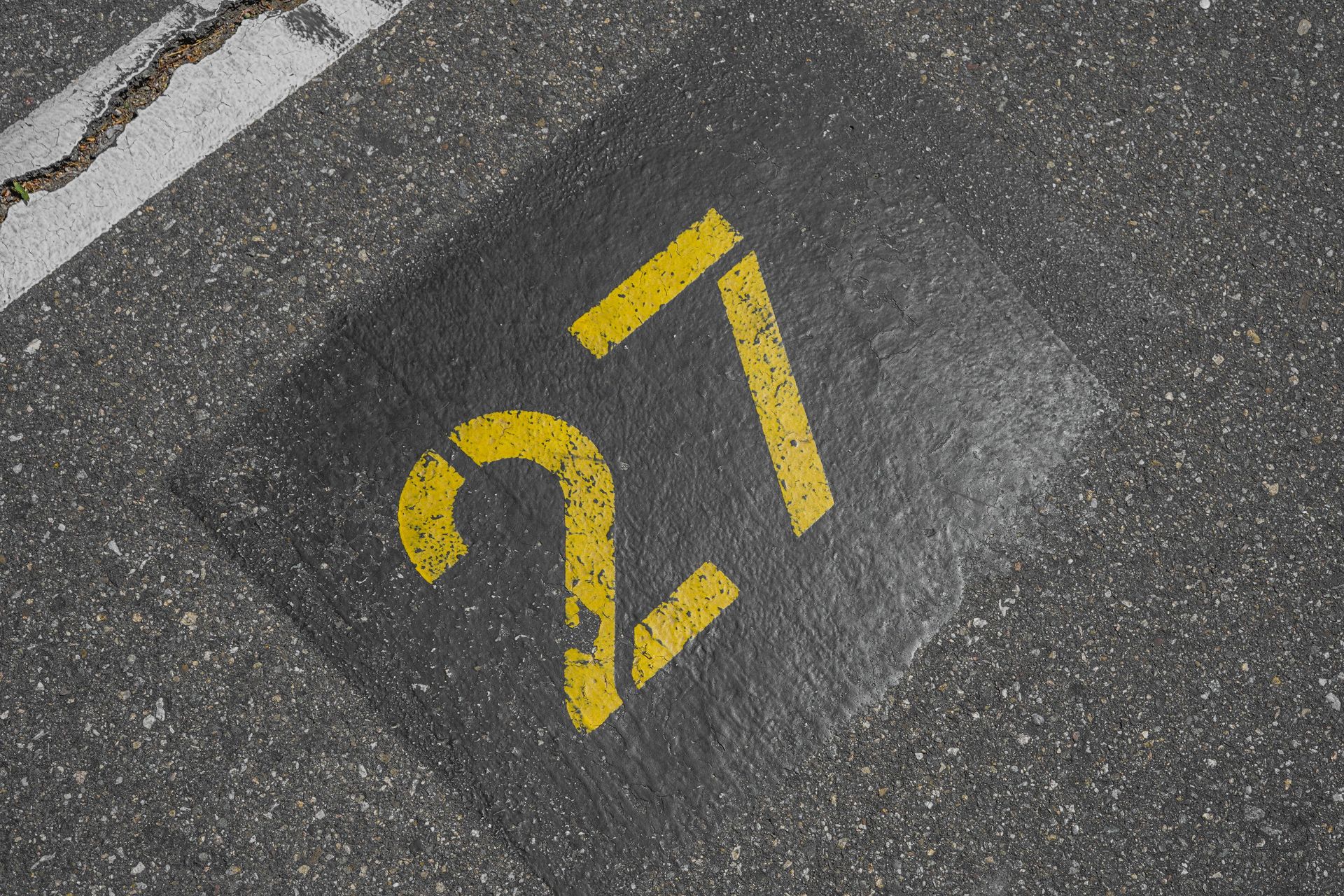 Close-up of the number 27 on asphalt in a parking lot, showing urban street details.